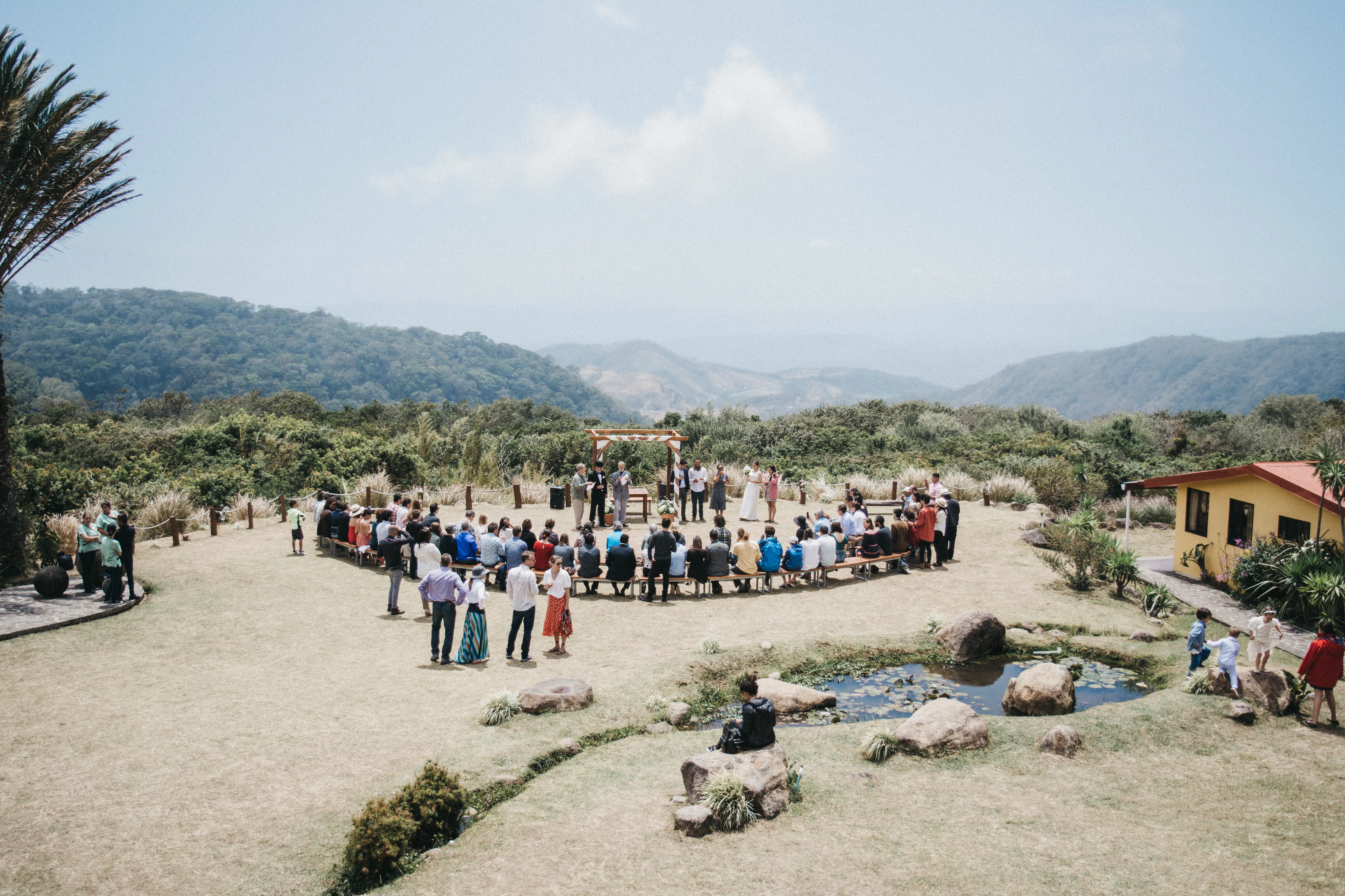 Visitors and guests watch as a bride and groom say their vows. Beyond the ceremony you can see beautiful mountain views and a clear sky.